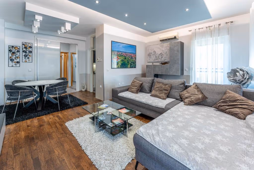 View down a hallway with light gray flooring, wooden door frames, an open wooden door on the right, and a glimpse of a modern living room.